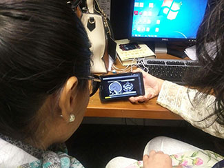 Two researchers seated with backs to camera in front of a computer view a video of brain scans on a mobile device