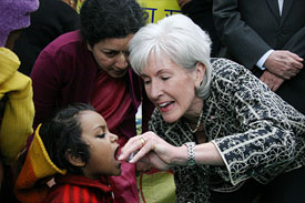 Kathleen Sebelius administers polio vaccine to young child, woman looks on closely from behind
