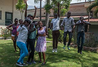 Group of teenagers in outdoor courtyard in Haiti pose for camera, some jump and raise hands.