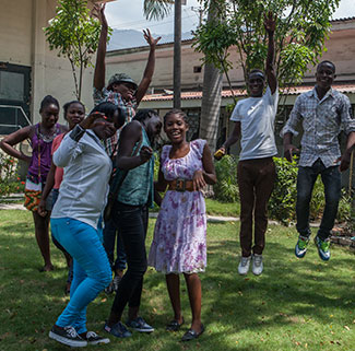 Group of teenagers in outdoor courtyard in Haiti pose for camera, some jump and raise hands