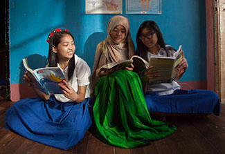 Three teenage girls seated on floor read from lesson books