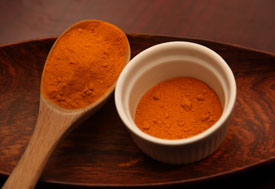 Close up of turmeric, an orange powder, in a small dish with a large wooden mixing spoon