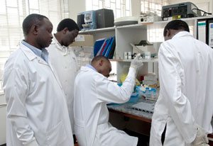Group of researchers in lab coats, one seated inserts samples into vials, three others observe