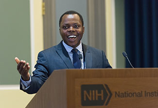 Dr. Jean Utumatwishima speaks from an NIH podium in a conference room