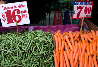 Large piles of green beans and carrots on display at outdoor market with signs showing prices