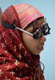 Young girl wearing head scarf wears large eye exam glasses over head to test vision with different lenses