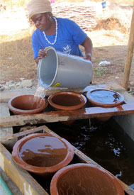 A woman pours water into a household water container with a clay water filter