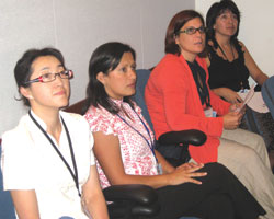 Photo: Four women scholars, seated, attentively listen to speaker