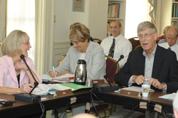 Dr. Francis Collins, seated at a panel table in a conference room to the right of two women, speaks into a microphone