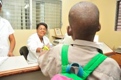 Photo: a child with his back to the camera hands a sample to a nurse behind a desk