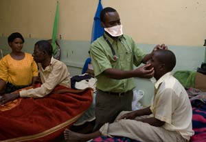 Photo: male doctor wearing a facemask, standing, examines a male patient, seated on hospital bed