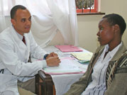 Photo: Dr. Gerald Bloomfield speaks to young male patient, both seated, a table covered with papers between them 
