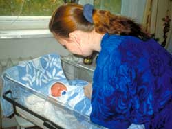 Photo: A woman nurse bends over a newborn in a plastic hospital crib