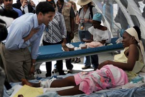 Photo: Rajiv Shah leans in to speak to a Haitian woman on an a hospital bed whose leg is bandaged and braced