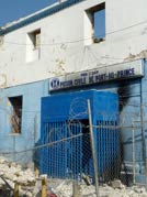 outside of concrete building, sign over door reads Prison Civile de Port-au-Prince, rubble covers ground