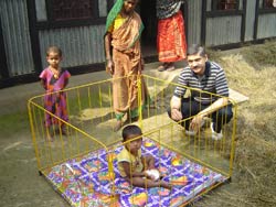 PHOTO: Dr. Hydner squats next to a toddler in a yellow metal playpen, another toddler and two women in wrap dresses look on