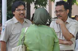 Photo: Dr Irmansyah and another man, both dressed in tan uniform shirts and facing camera, speak to woman with green head scarf