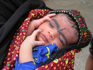 Photo: Pakistani baby sleeping wrapped in blanket with grey surma eye makeup along eyebrows and forehead