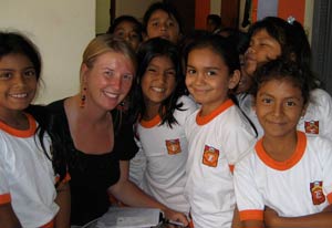 Photo: Catherine Pastorius seated surrounded by many young Peruvian girls in soccer jerseys, all smiling.
