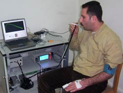 Man seated in chair observes computer screen and equipment as he inhales on a cigarette