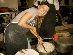 PHOTO: Dr. Elizabeth Vaughan, smiling, stirs large metal pot full of white porridge with large wooden spoon