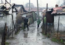 Muddy path full of puddles between shantys in a ghetto in Sophia, Bulgaria, rain falls, two people run away from camera