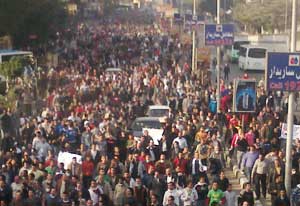 Crowded street in Egypt packed with protesters walking, some abandoned cars in road, some carry signs