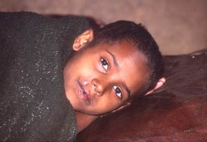 Young Ethiopian child rests on its side, wrapped in a blanket, looks into camera