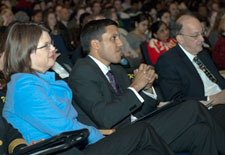 Dr. Rajiv Shah sits in audience seated between Dr. Roger Glass and Lois Quam, full audience in background
