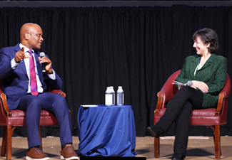 Ambassador Dr. John Nkengasong speaks with U.S. National Institutes of Health Director Dr. Monica Bertagnolli on the stage of the Ruth Kirschstein Auditorium on the NIH campus on June 6, 2024. Nkengasong is dresed in blue suit and pink tie; Bertagnolli wears vivid green and black. 