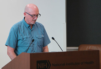 This photo shows Patrick Duffy of NIAID standing at a podium. He is wearing glasses and a light blue shirt.