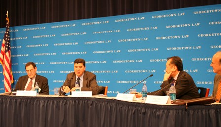 Four panelists address issues, a blue Georgetown Law backdrop in white letters and American flag is seen on the left.