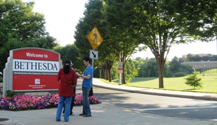 Three Fogarty scholars standing in front of the Welcome to Bethesda sign near the NIH campus. Part of the campus can be seen off to the right side.