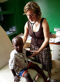 Dr Manning in an exam room with stethoscope in ears holds it to a young boy’s back, she looks down at him