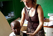Dr Manning in an exam room with stethoscope in ears holds it to a young boy’s back, she looks down at him