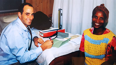 Dr. Thomas Gaziano seated in exam room and taking notes next to smiling female patient