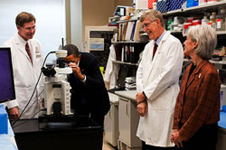 PHOTO: President Obama look into a microscope in a laboratory at NIH, while Dr. Marston Linehan, NIH Director Dr. Francis Collins and HHS Secretary Kathleen Sebelius look on.